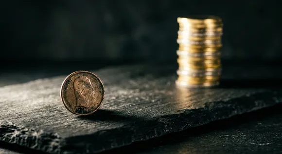 Conceptual still life showing a single coin contrasted against a large stack of coins, representing per-capita income disparity