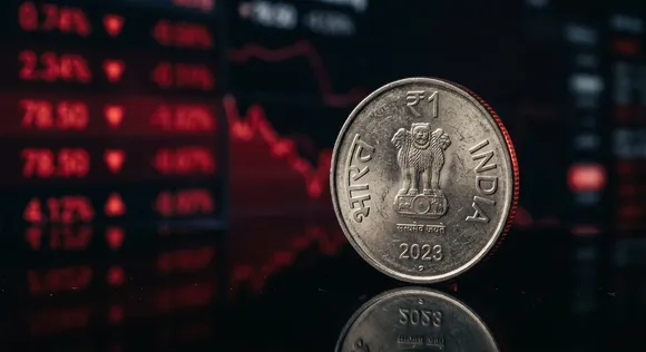 Indian Rupee coin on a reflective surface with a blurred red financial ticker in the background